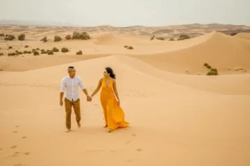 A couple enjoying a romantic walk in the golden sand dunes during a 3 day Morocco desert tour from Marrakesh.