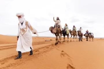 A Berber guide leading a camel caravan through the Sahara Desert during a 3 Days From Fes to Merzouga tour, offering an unforgettable desert adventure.