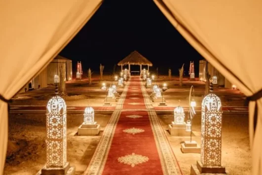 Luxury desert camp in Merzouga, Morocco, illuminated by traditional lanterns at night, offering an authentic stay during a 5 Days Tour From Marrakech To Merzouga Desert.