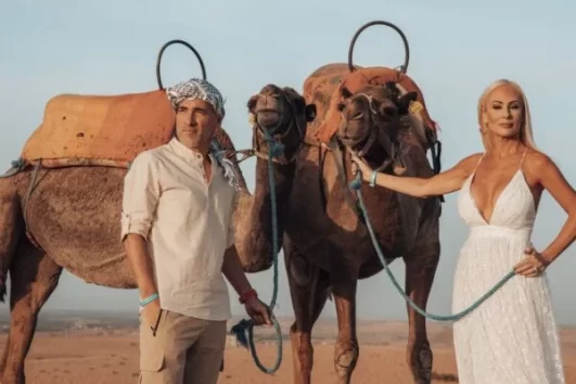 A couple posing with camels in the Moroccan desert, symbolizing the adventure of a Marrakech to Fes Desert Tour 4 Days with camel trekking.