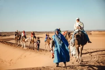 Travelers enjoying a camel trek through the golden Sahara dunes with a local Berber guide during the Fes to Marrakech Desert Tour 3 Days.