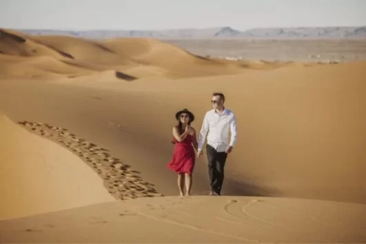 A couple walking hand in hand on the golden sand dunes of Merzouga, enjoying the serene desert landscape during their Errachidia to Merzouga tour.