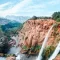 Stunning view of Ouzoud Waterfalls, one of the best places to see in Morocco, surrounded by lush greenery and red cliffs