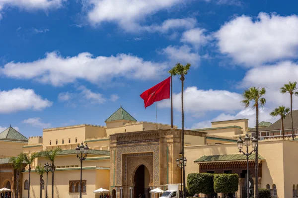 A historic Moroccan palace with intricate architecture, palm trees, and the national flag waving under a bright blue sky – Morocco Travel Tips.